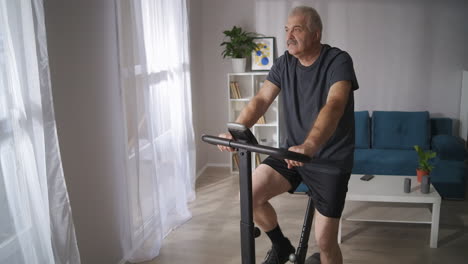 athletic-middle-aged-man-is-training-on-exercycle-in-living-room-healthy-lifestyle-at-isolation-period-during-pandemic-keeping-good-physical-condition-at-middle-age